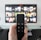 A person holds a remote control in front of a TV displaying a streaming platform interface with various movie and show thumbnails. The room includes a desk with two small lamps on either side of the TV.
