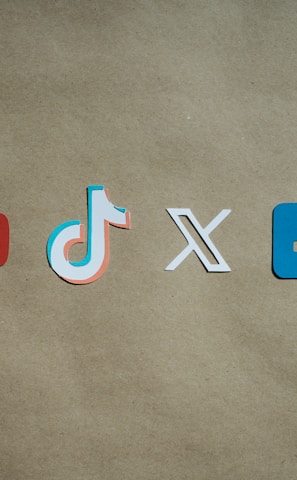 Four social media platform logos are arranged on a brown background. From left to right, the logos are for YouTube in red, TikTok in a combination of red, blue, and white, X in white, and Facebook in blue.